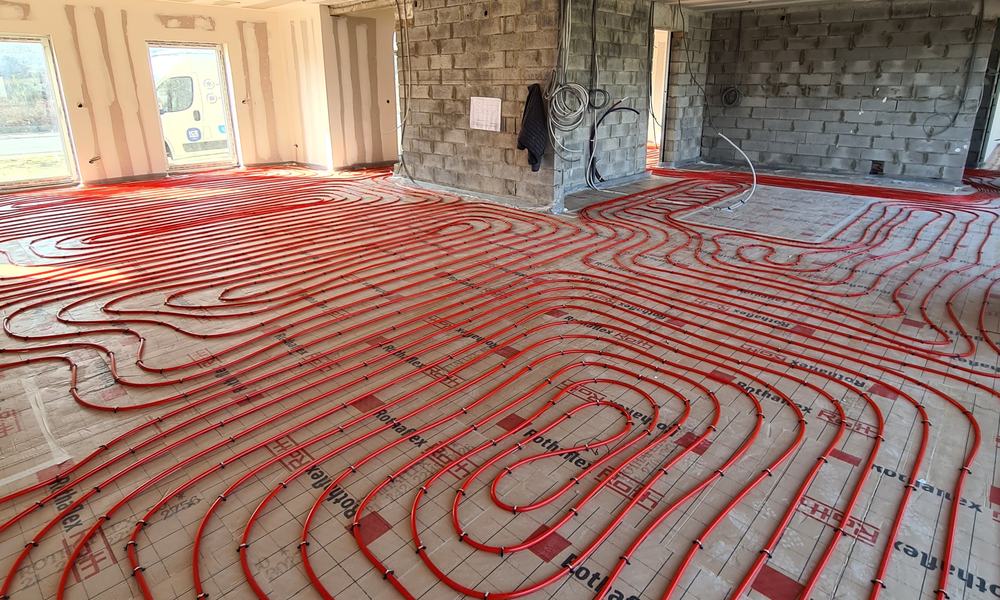 Tubes de plancher chauffant rouges posés en boucles sur l’isolant dans un grand séjour en construction